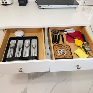 En skuffe med bestik, en servietholder med kaffemotiv og en mindre hårdelement på en bordplade.