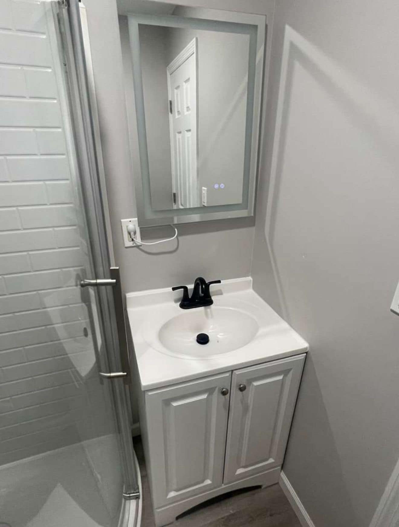 Une salle de bain avec un lavabo blanc, un miroir au-dessus et une porte de douche.