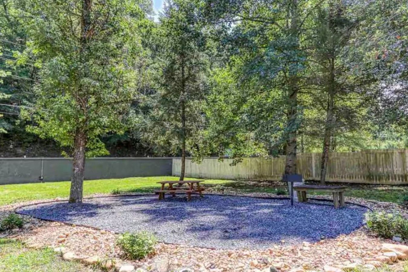 A park area with a picnic table and benches surrounded by gravel and trees.
