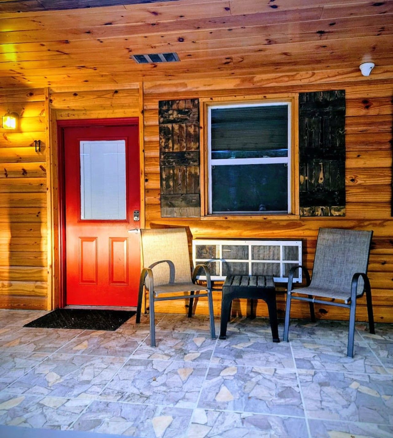A wooden cabin with a red door, a window with a view, and a stone-tiled floor.