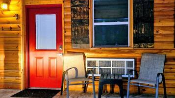 A wooden cabin with a red door, a window with a view, and a stone-tiled floor.
