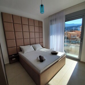 Ett modernt hotellrum med en stor säng, en sänggavel, ett nattduksbord och utsikt över staden genom ett stort fönster.