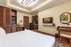 Une chambre d’hôtel avec un grand lit, un bureau avec une chaise, une kitchenette et une salle de bain avec douche.