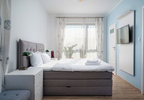 Une chambre moderne avec un lit, des tables de chevet, une télévision et une fenêtre avec des rideaux.