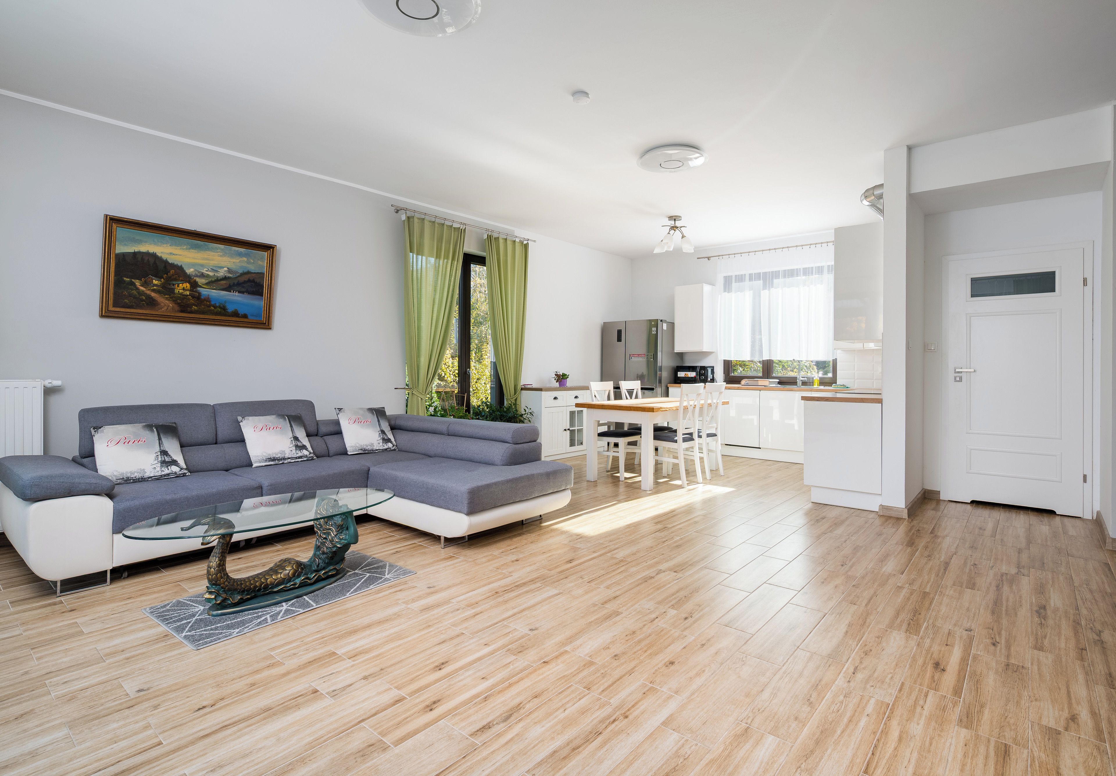 Een moderne woonkamer met een grijze bank, een glazen salontafel en een schilderij aan de muur.
