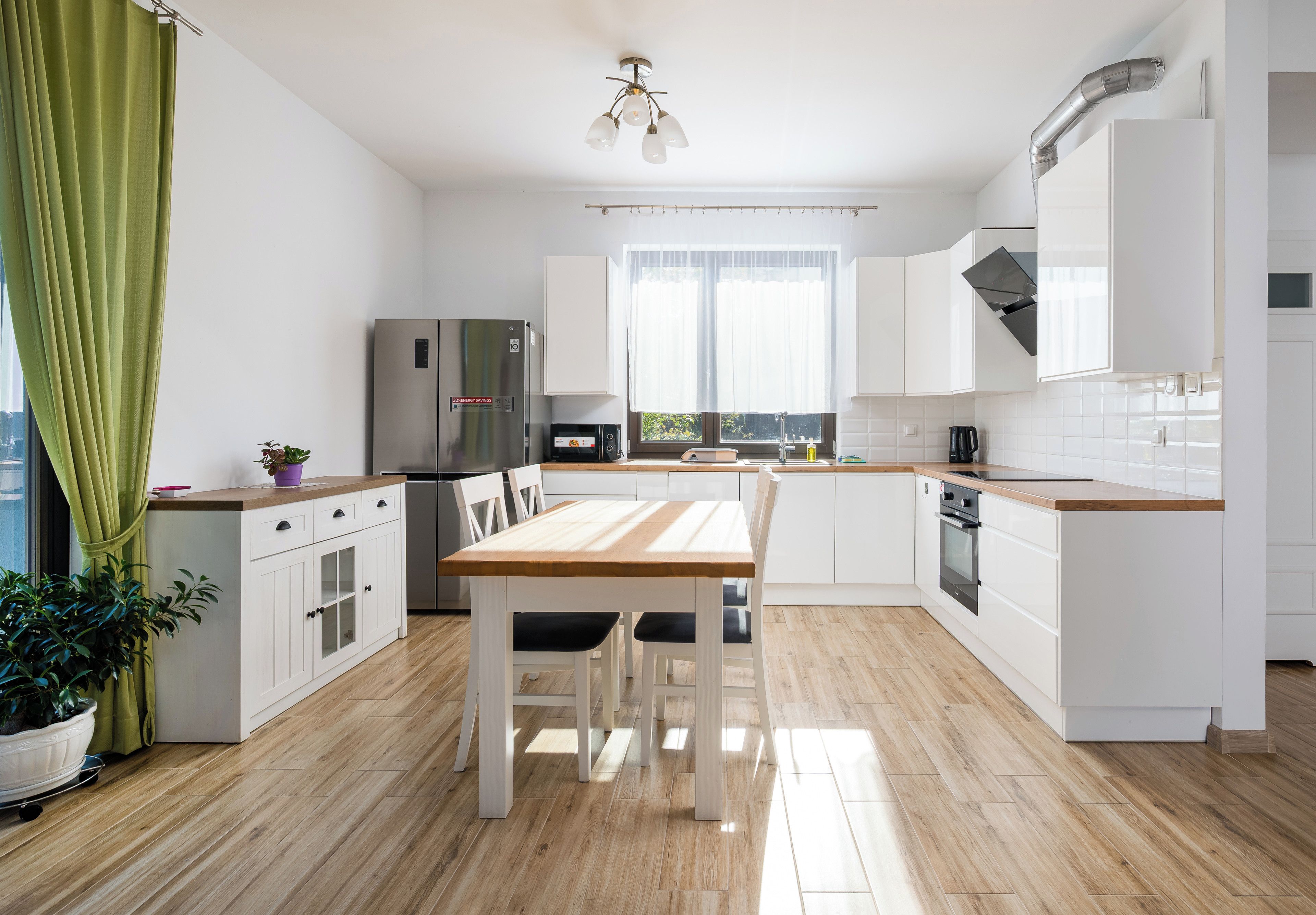 Een moderne keuken met witte kastjes, een houten eettafel en een inbouwoven.
