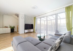 Un salon moderne avec un ensemble de canapés, une table basse en verre et un téléviseur posé sur un meuble blanc.