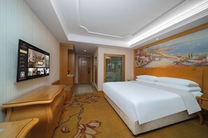 A hotel room with a bed, a desk, a chair, a painting on the wall, and a view of the sea. - Vienna Hotel GZ Baiyun Airport North (guangzhou)