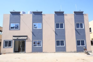 Um edifício de vários andares com fachada plana, entrada visível e uma placa com a inscrição 'VIAY DARSHAN'.