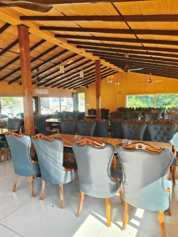 A spacious indoor dining area with a long wooden table and matching chairs, supported by wooden beams and columns.