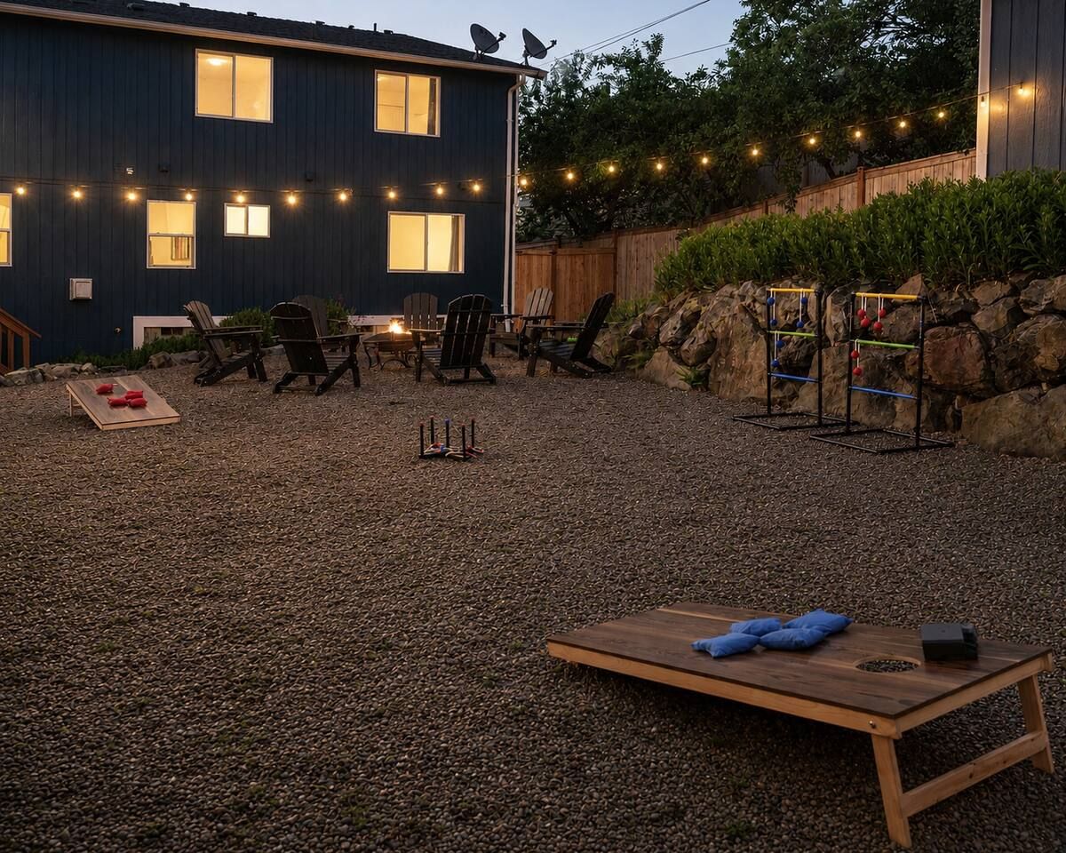 A backyard with a gravel surface, outdoor furniture, a ping pong table, and a house with string lights.