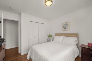 A bedroom with a bed, a nightstand, a bedside table, a wall-mounted light fixture, and a door. - New Spacious Luxe Home | Views & Game Room! (Tacoma)