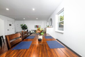 Een ruime kamer met een houten eettafel, blauwe matten en een potplant.