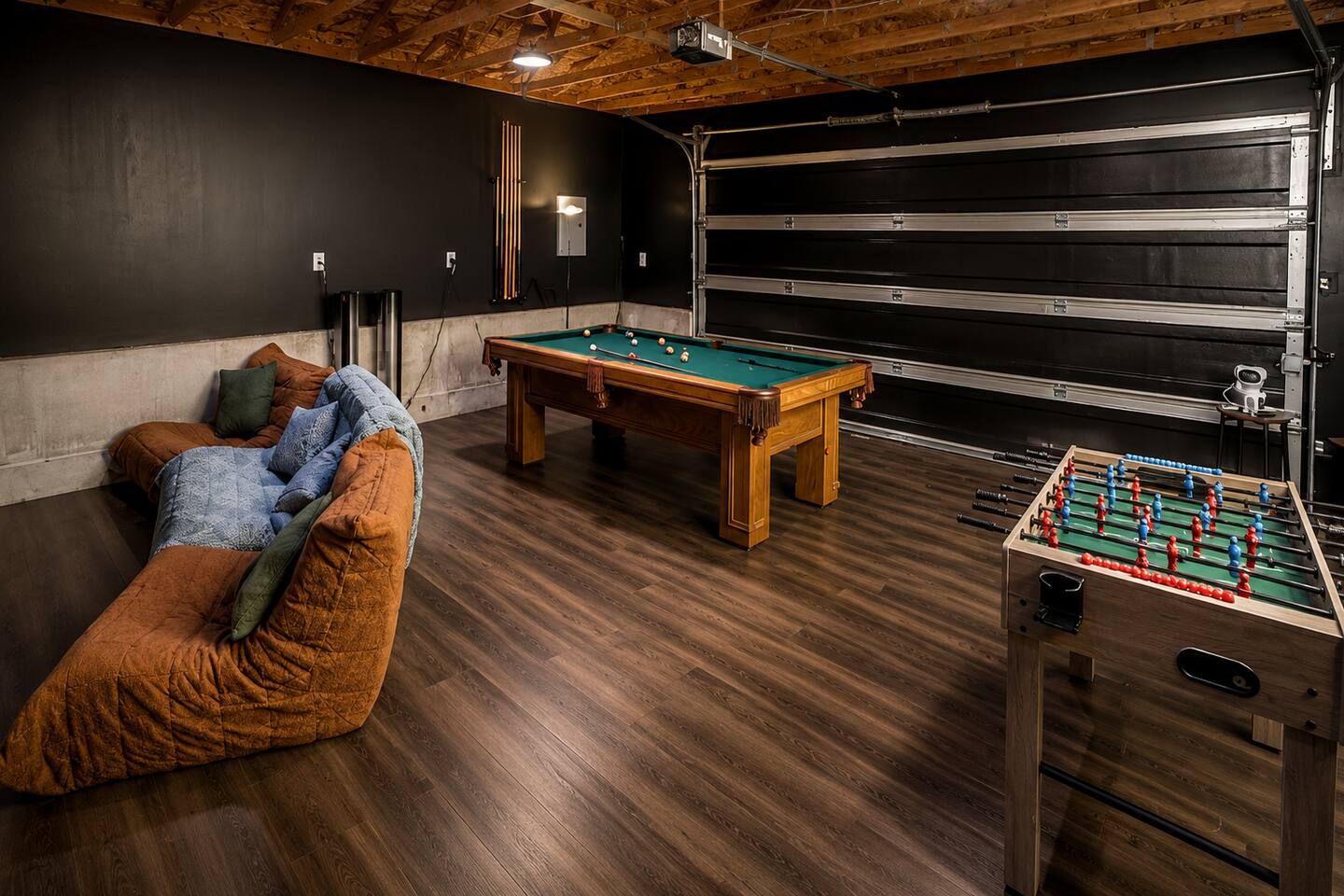 A room with a pool table, a foosball table, and a sofa.