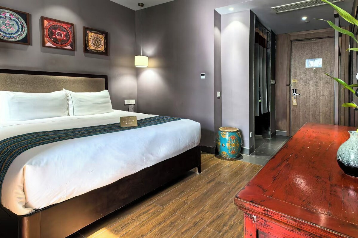Quarto de hotel com cama, mesas de cabeceira, um vaso decorativo e uma porta para outro cômodo.