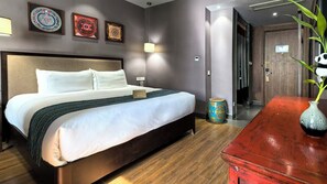 Quarto de hotel com cama, mesas de cabeceira, um vaso decorativo e uma porta para outro cômodo.
