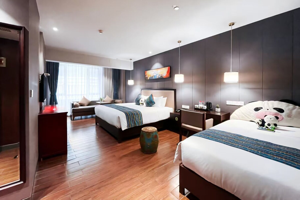 Quarto de hotel com duas camas, um sofá, uma mesa de centro e um vaso decorativo.