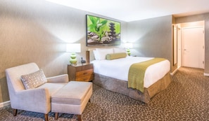 Een hotelkamer met een bed, een stoel, een nachtkastje en een schilderij aan de muur.