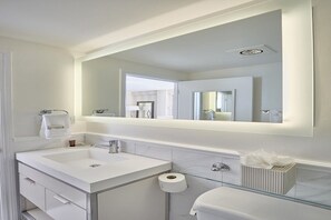 Et moderne badeværelse med et stort spejl, en hvid vask og et toilet med glaslåge.