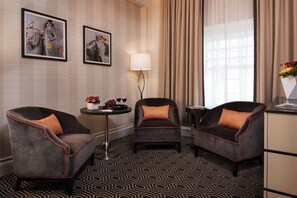 Ein Hotelzimmer mit zwei Sesseln, einem runden Tisch, einer Lampe und Bildern an der Wand.