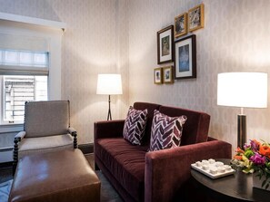 Ein Hotelzimmer mit braunem Ledersofa, einem passenden Sessel, einem kleinen Tisch mit Tabletts für Toilettenartikel und einem Fenster mit Jalousien.