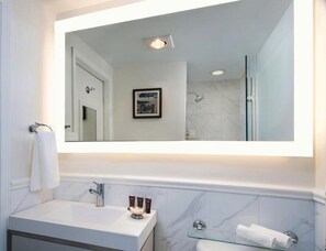 Et moderne badeværelse med et stort spejl, en vask med toiletartikler og en brusekabine i glas.
