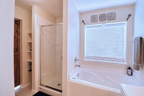 Ein Badezimmer mit Duschkabine aus Glas, einer Badewanne und einem Fenster mit Jalousien.
