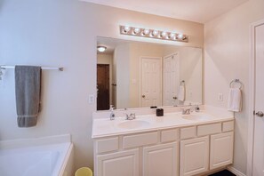A bathroom with a double sink vanity, a large mirror with lights, and a towel rack. - Cozy Katy 3BR | Fireplace, Backyard & Game Room (Katy)