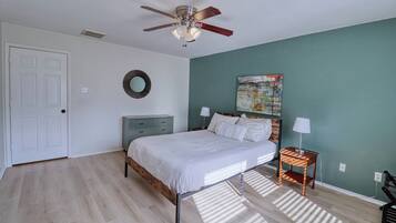 Een slaapkamer met een bed, nachtkastjes, een plafondventilator, een deur en een spiegel aan de muur.