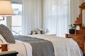 A hotel room with a bed, a lamp, a dresser, and a view of the outdoors.