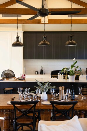 A modern kitchen with dark cabinetry, pendant lighting, and a dining area set for a meal.
