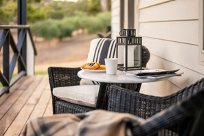 A wicker chair with a cushion, a small round table with a white mug and a plate of pastries, and a black lantern on the table.
