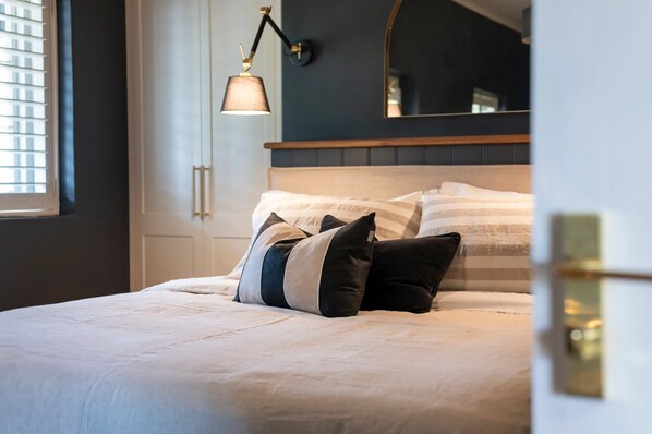 A neatly made bed with a white comforter and multiple pillows, a bedside lamp, and a large mirror above the bed.