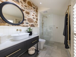 A bathroom with a stone wall, a white sink, a mirror, a glass shower enclosure, and a towel rack.