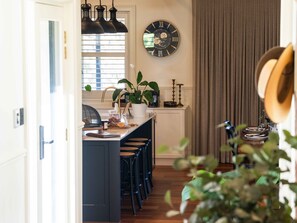 A kitchen with a central island, bar stools, a clock, and a window with blinds.