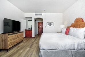 Una habitación de hotel con una cama grande, un aparador de madera, un televisor y una puerta que da a otra habitación.