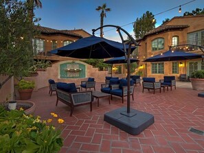 Ein Terrassenbereich im Freien mit Sitzgelegenheiten und Sonnenschirmen, umgeben von einer Ziegelmauer und Kübelpflanzen.