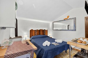 Habitació d'hotel amb llit, taula de nit, làmpada i safata de petit esmorzar amb pastissos.