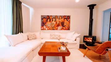 Una sala de estar con sofá, mesa de centro, cuadro y estufa de leña.