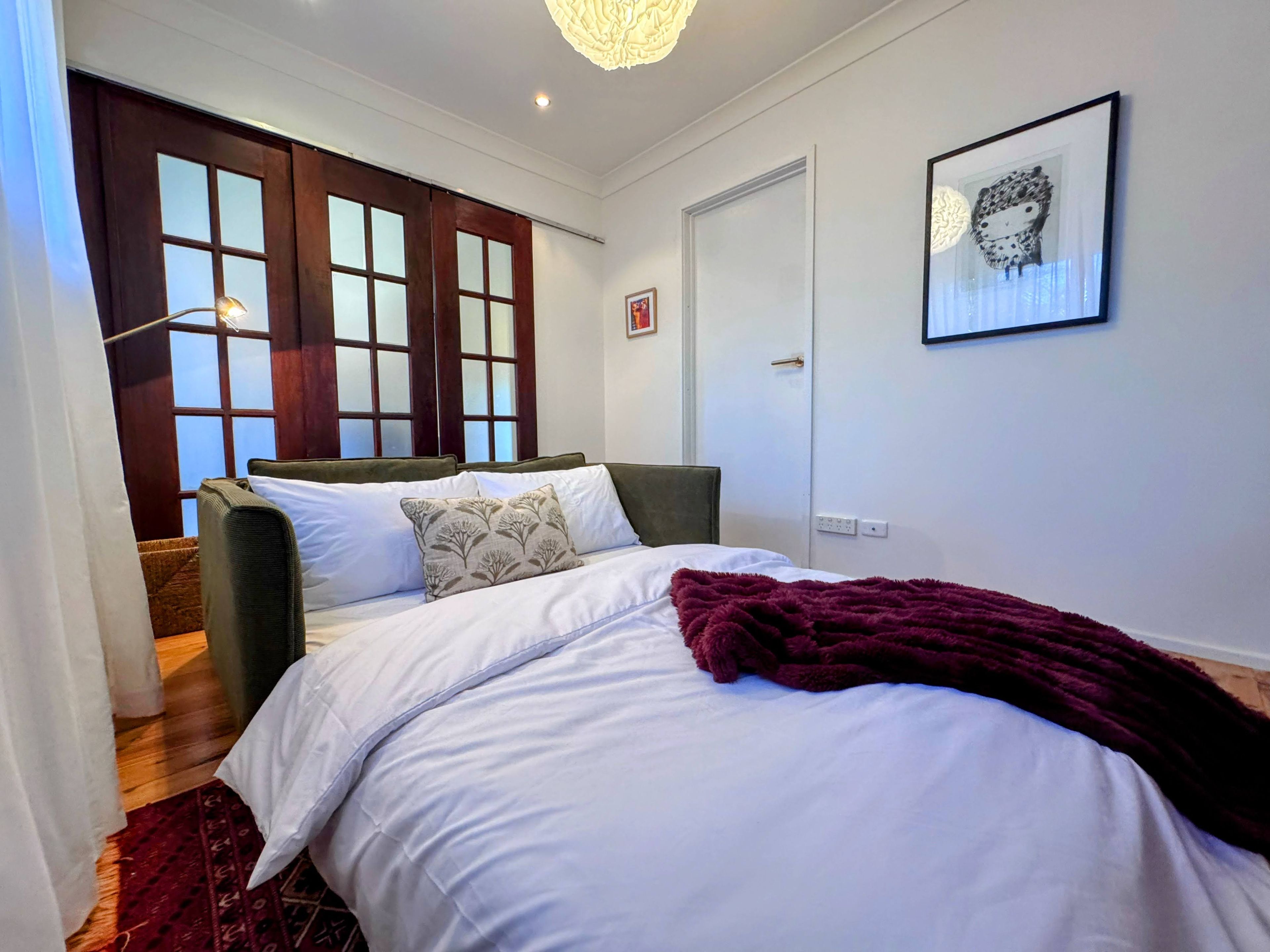 A bedroom with a bed, a window, a door, and a wall-mounted artwork.