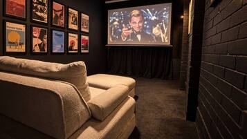 A cozy room with a large screen for viewing, a comfortable sofa, and a wall adorned with framed movie posters.