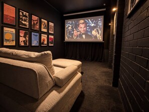 A cozy room with a large screen for viewing, a comfortable sofa, and a wall adorned with framed movie posters.