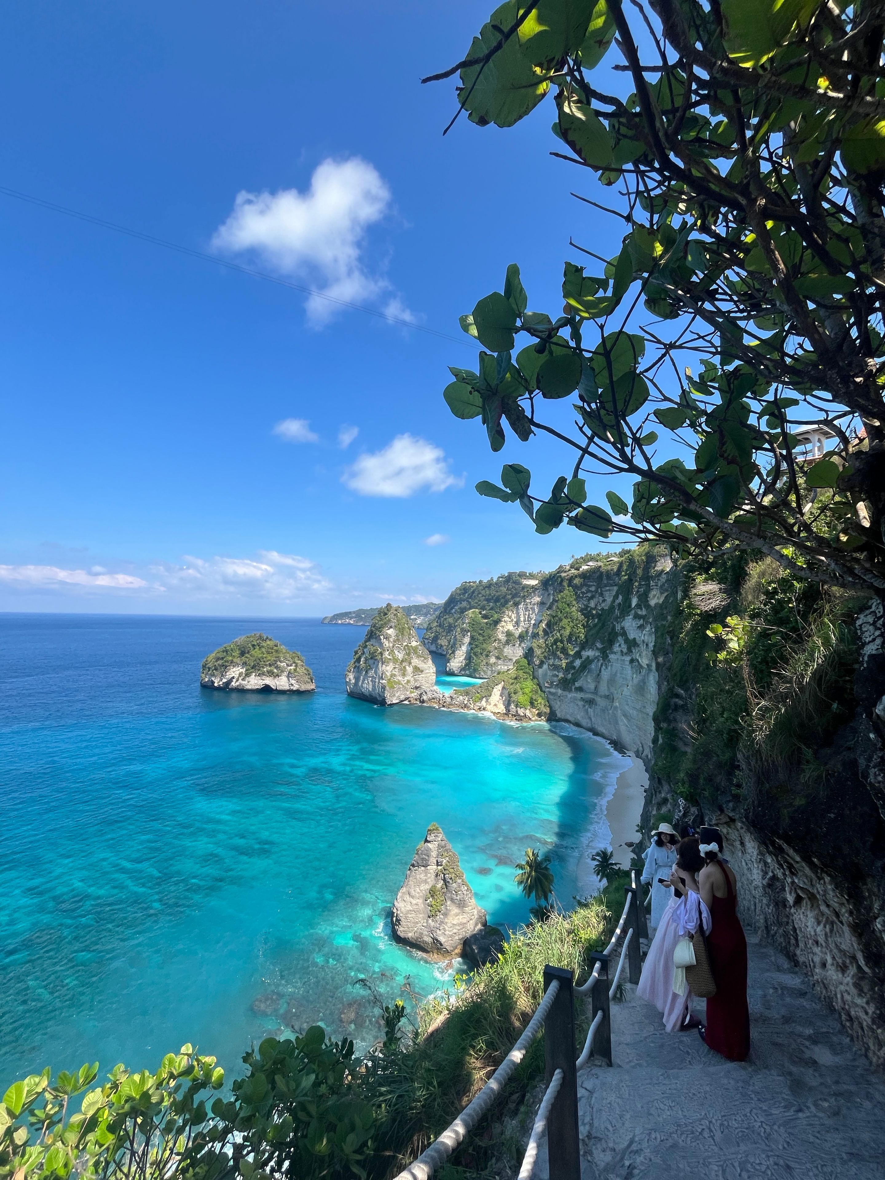 Paisagem costeira com águas azul-claras, falésias rochosas e um caminho que leva a uma praia.