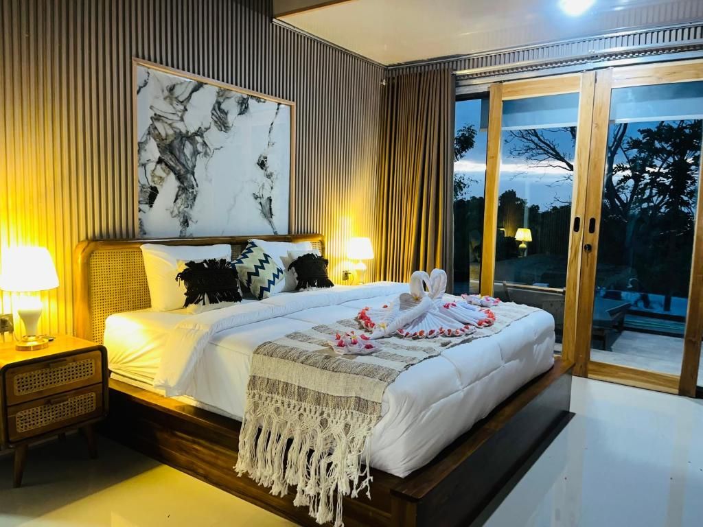 Une chambre d’hôtel avec un grand lit, une table de chevet avec une lampe, un tableau accroché au mur et une porte-fenêtre coulissante donnant sur un espace extérieur.