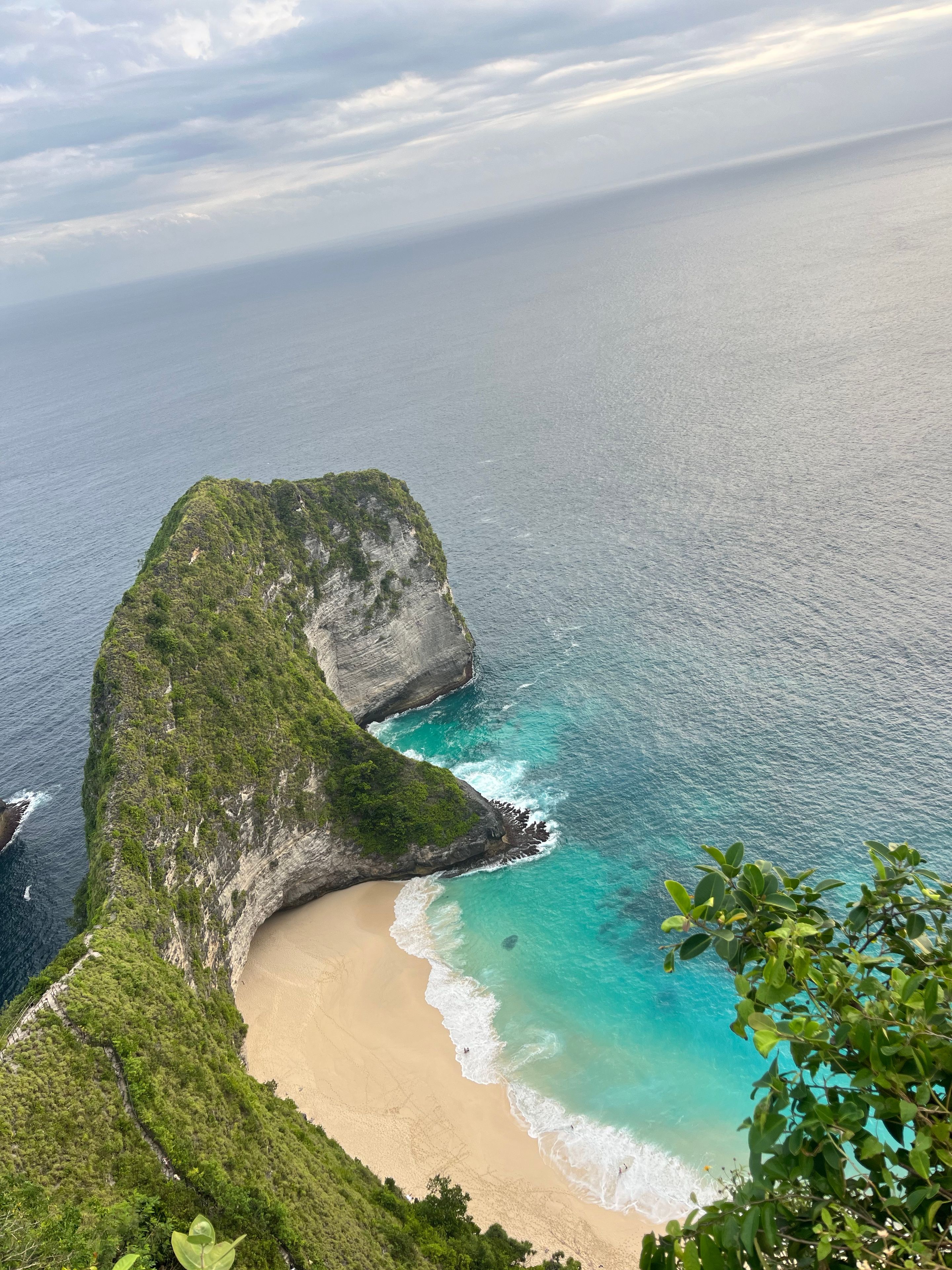 Paisagem costeira com um penhasco imponente, uma praia arenosa e águas turquesa cristalinas.