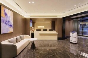 Un espace d’accueil d’hôtel comprenant un comptoir de réception, un canapé, une petite table et un robot.