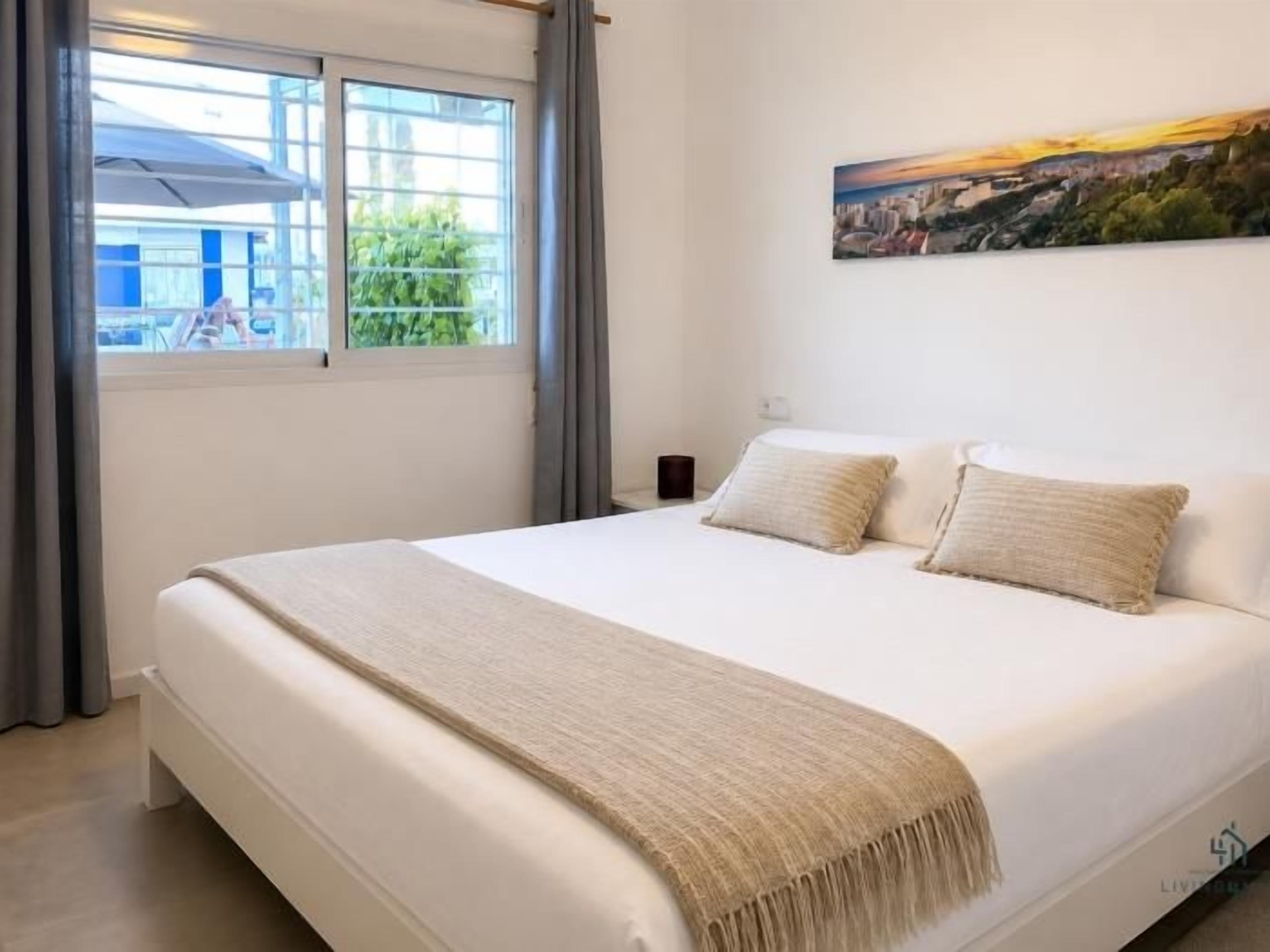 Un dormitorio con una cama grande, una ventana con cortinas y un cuadro de un paisaje urbano en la pared.