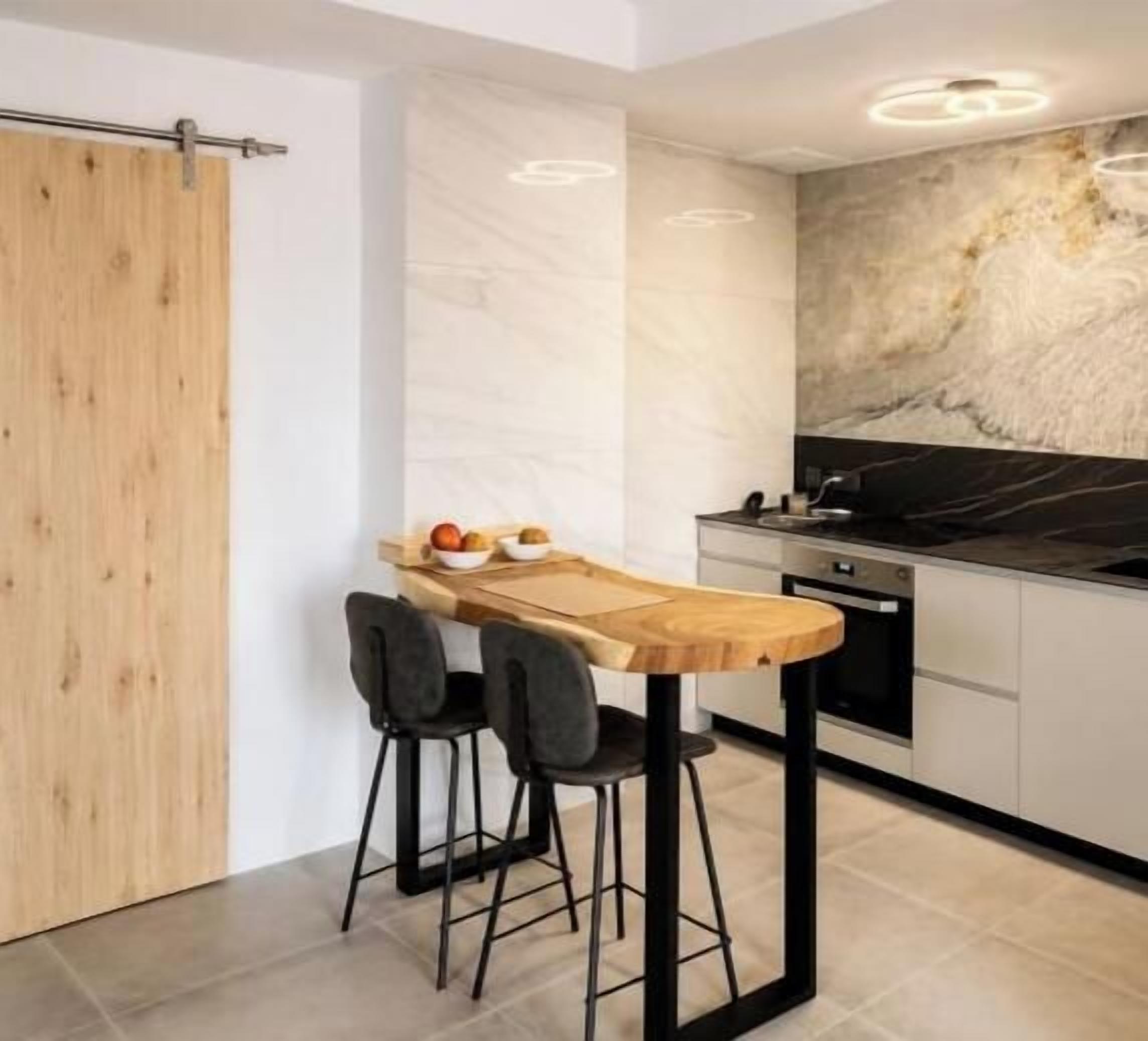 A modern kitchen with a wooden bar counter, two bar stools, a marble backsplash, and a black stove.