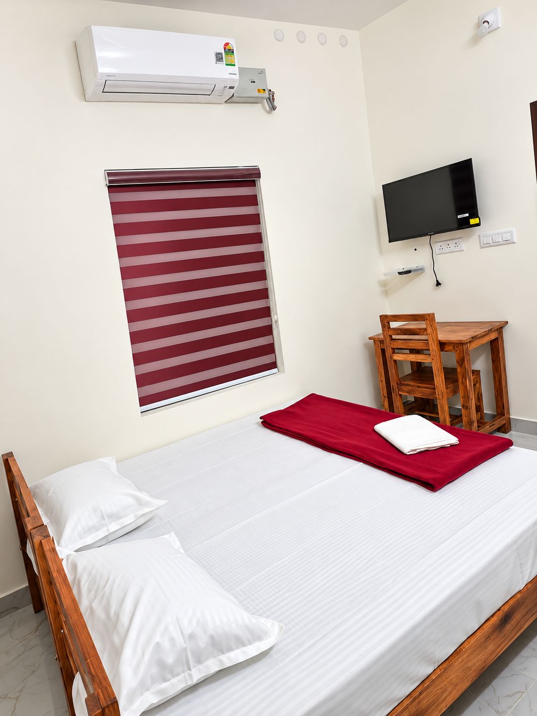 Une chambre d’hôtel équipée d’un lit, d’une télévision, d’une fenêtre avec stores et d’un appareil de climatisation.