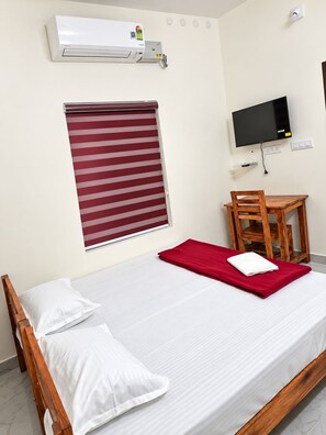 Ein Hotelzimmer mit Bett, Fernseher, einem Fenster mit Jalousien und einer Klimaanlage.